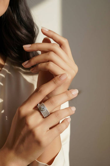 Close-up of a hand wearing a diamond ring with a blurred background. Inara rhodium plated pavé wide band ring on hand in natural light modern desi ring by Inaury