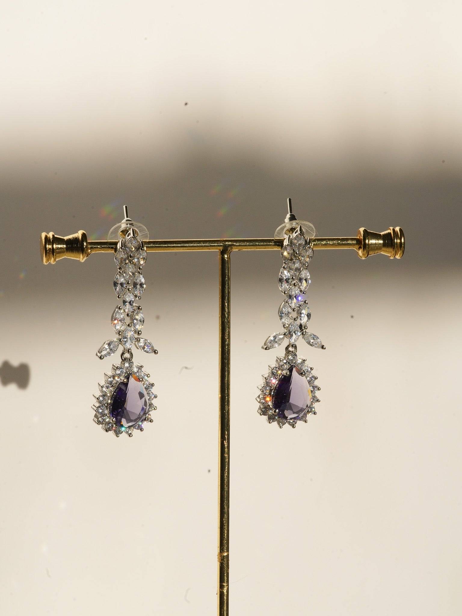 Lina Long Diamante Accent AD Necklace Set - Rhodium-plated with white AD stones, featuring intricate patterns and pendant-like centerpiece, available in silver & sapphire blue, silver & purple, and silver & citrine yellow, with matching dangling earrings.