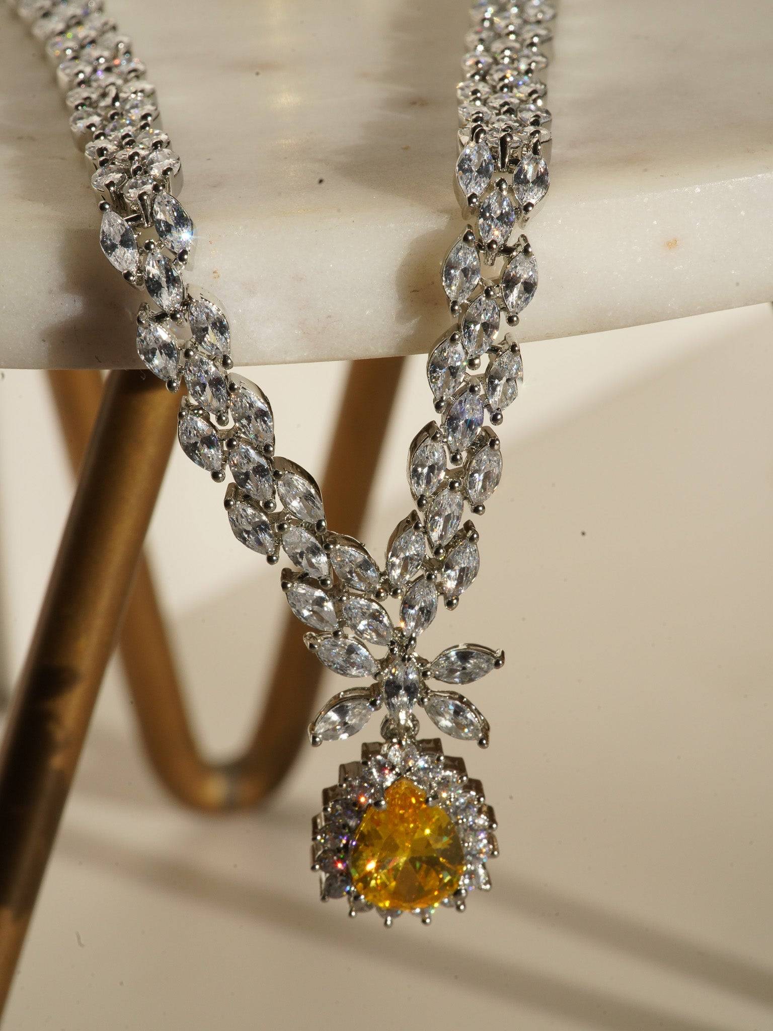 Lina Long Diamante Accent AD Necklace Set - Rhodium-plated with white AD stones, featuring intricate patterns and pendant-like centerpiece, available in silver & sapphire blue, silver & purple, and silver & citrine yellow, with matching dangling earrings.
