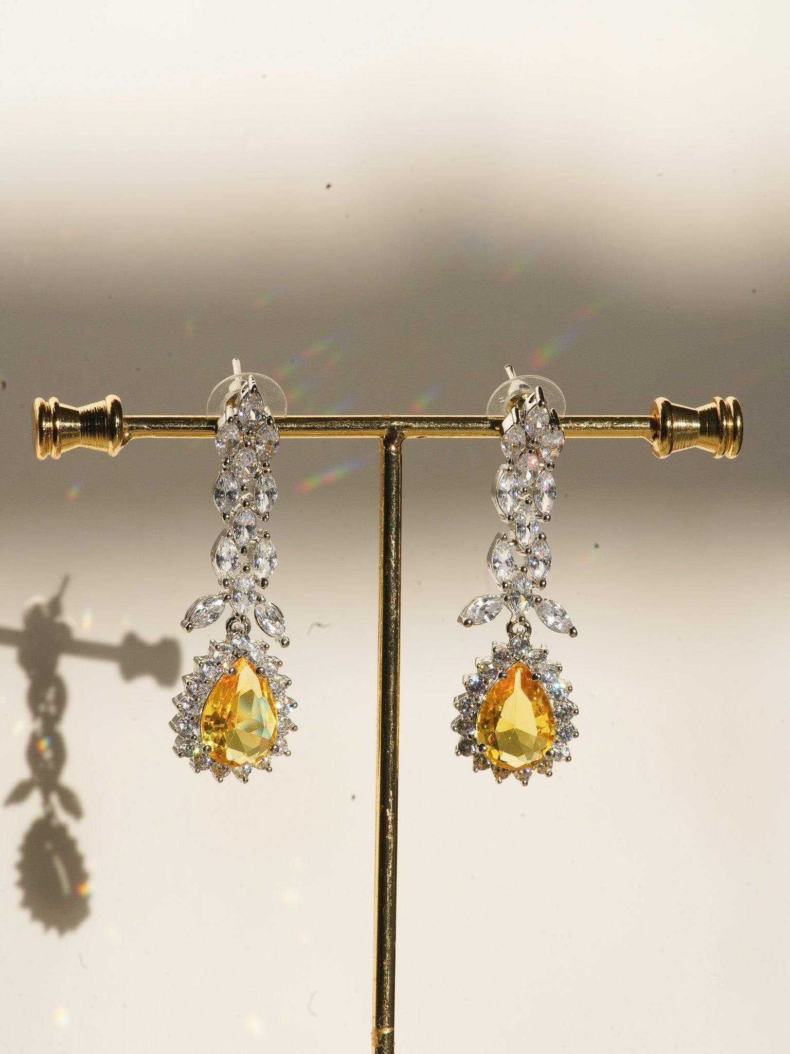 Lina Long Diamante Accent AD Necklace Set - Rhodium-plated with white AD stones, featuring intricate patterns and pendant-like centerpiece, available in silver & sapphire blue, silver & purple, and silver & citrine yellow, with matching dangling earrings.