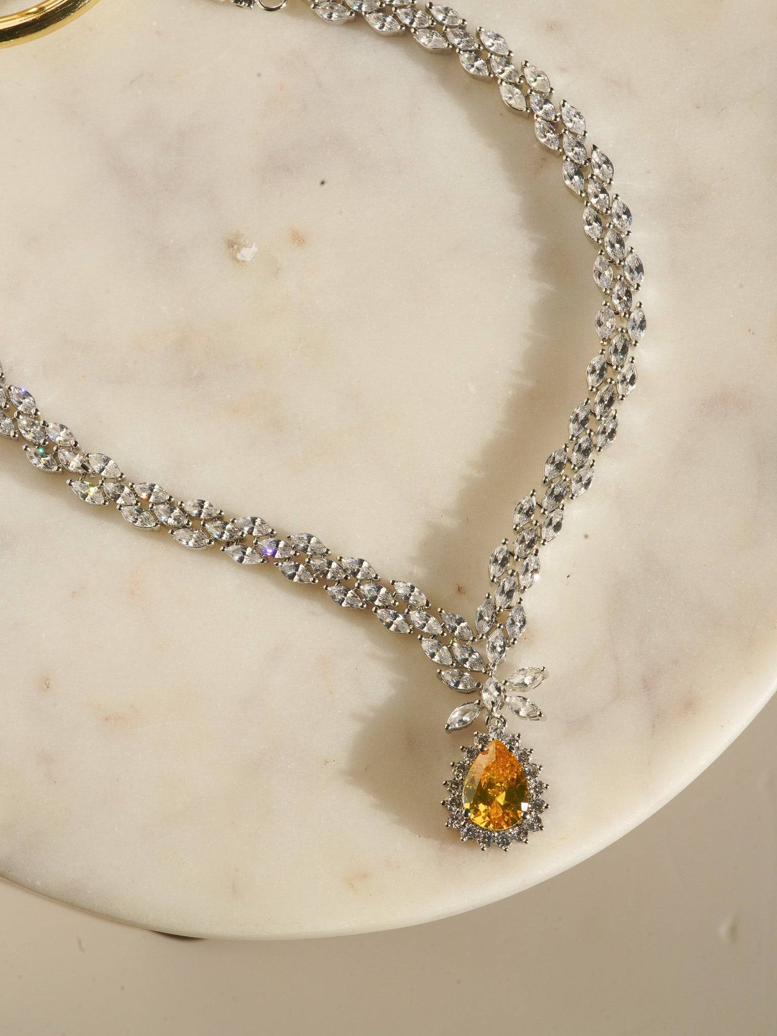 Lina Long Diamante Accent AD Necklace Set - Rhodium-plated with white AD stones, featuring intricate patterns and pendant-like centerpiece, available in silver & sapphire blue, silver & purple, and silver & citrine yellow, with matching dangling earrings.