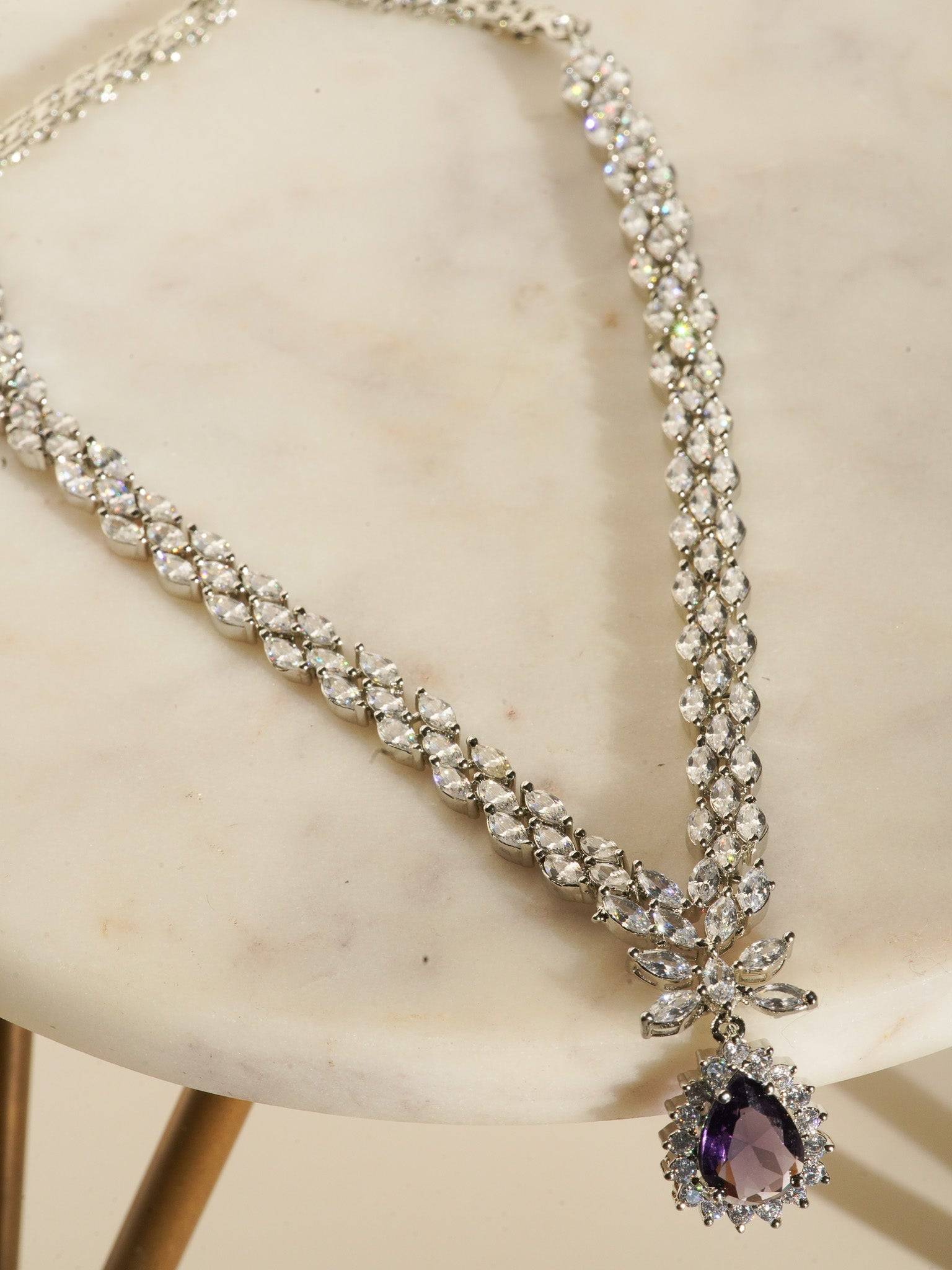 Lina Long Diamante Accent AD Necklace Set - Rhodium-plated with white AD stones, featuring intricate patterns and pendant-like centerpiece, available in silver & sapphire blue, silver & purple, and silver & citrine yellow, with matching dangling earrings.