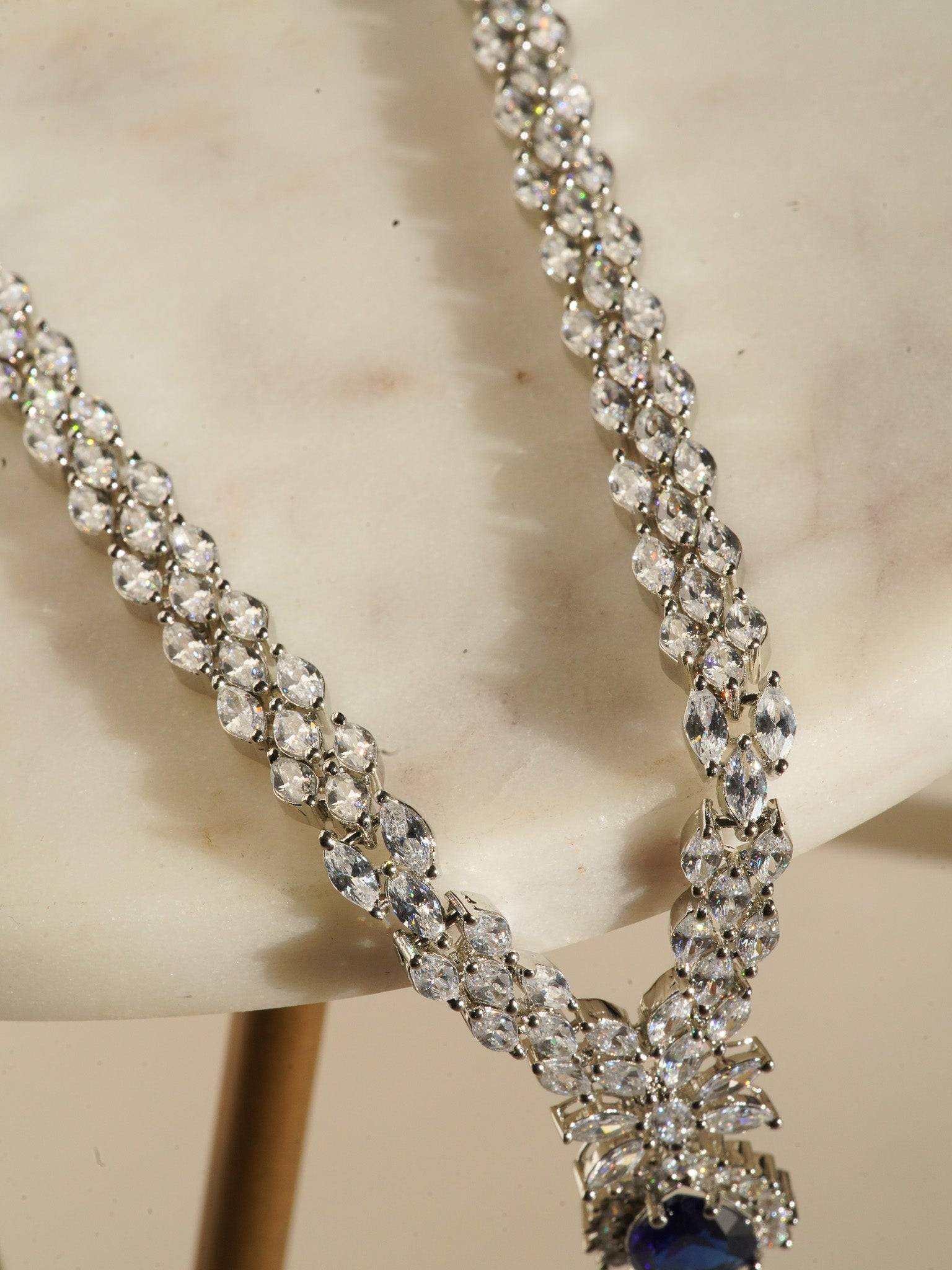 Lina Long Diamante Accent AD Necklace Set - Rhodium-plated with white AD stones, featuring intricate patterns and pendant-like centerpiece, available in silver & sapphire blue, silver & purple, and silver & citrine yellow, with matching dangling earrings.