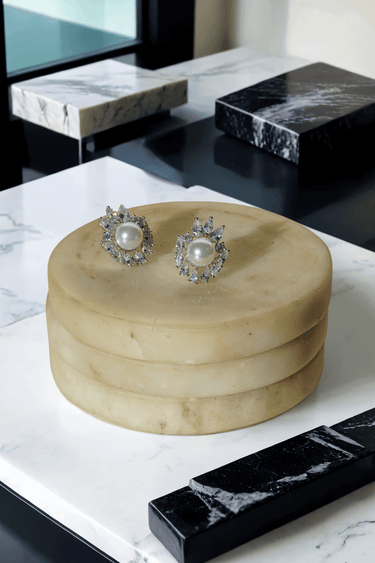 Close-up of Mayesha Pearl Earrings placed on a beige round stand, showcasing their floral CZ and freshwater pearl design.