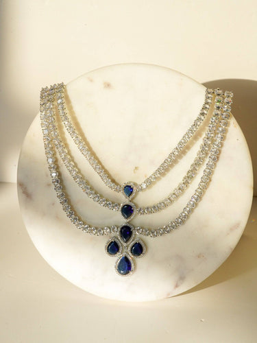 Niara Triple Layer Diamante Accent AD Necklace Set in gold or rhodium-plated silver finish with color options of silver & sapphire blue, silver & green, gold & green, and silver & ruby, featuring triple-layered chain links and matching statement earrings.
