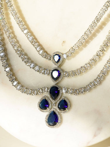 Niara Triple Layer Diamante Accent AD Necklace Set in gold or rhodium-plated silver finish with color options of silver & sapphire blue, silver & green, gold & green, and silver & ruby, featuring triple-layered chain links and matching statement earrings.