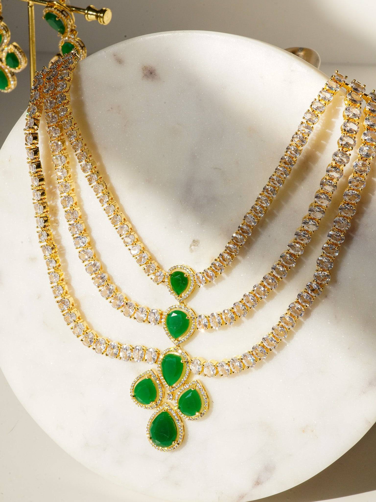 Niara Triple Layer Diamante Accent AD Necklace Set in gold or rhodium-plated silver finish with color options of silver & sapphire blue, silver & green, gold & green, and silver & ruby, featuring triple-layered chain links and matching statement earrings.