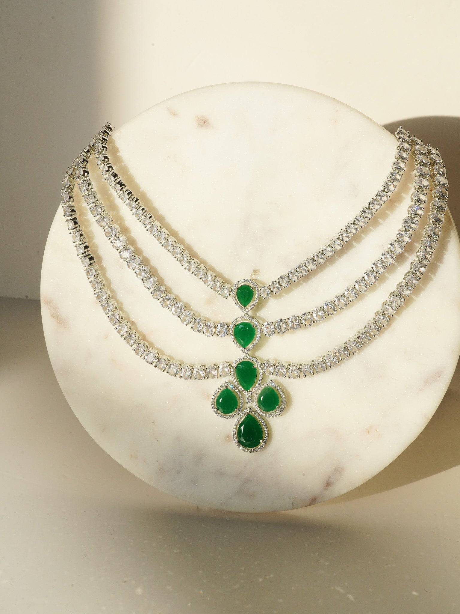 Niara Triple Layer Diamante Accent AD Necklace Set in gold or rhodium-plated silver finish with color options of silver & sapphire blue, silver & green, gold & green, and silver & ruby, featuring triple-layered chain links and matching statement earrings.