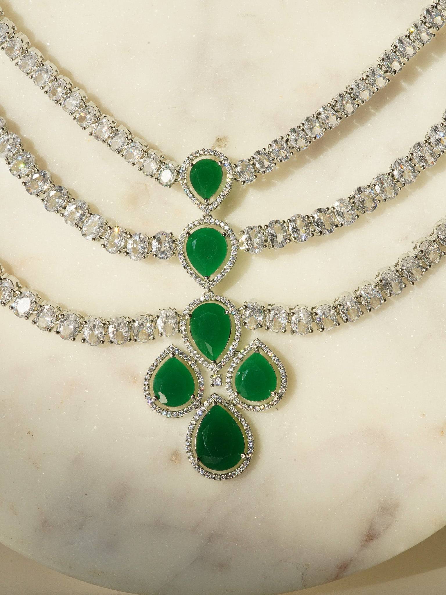 Niara Triple Layer Diamante Accent AD Necklace Set in gold or rhodium-plated silver finish with color options of silver & sapphire blue, silver & green, gold & green, and silver & ruby, featuring triple-layered chain links and matching statement earrings.