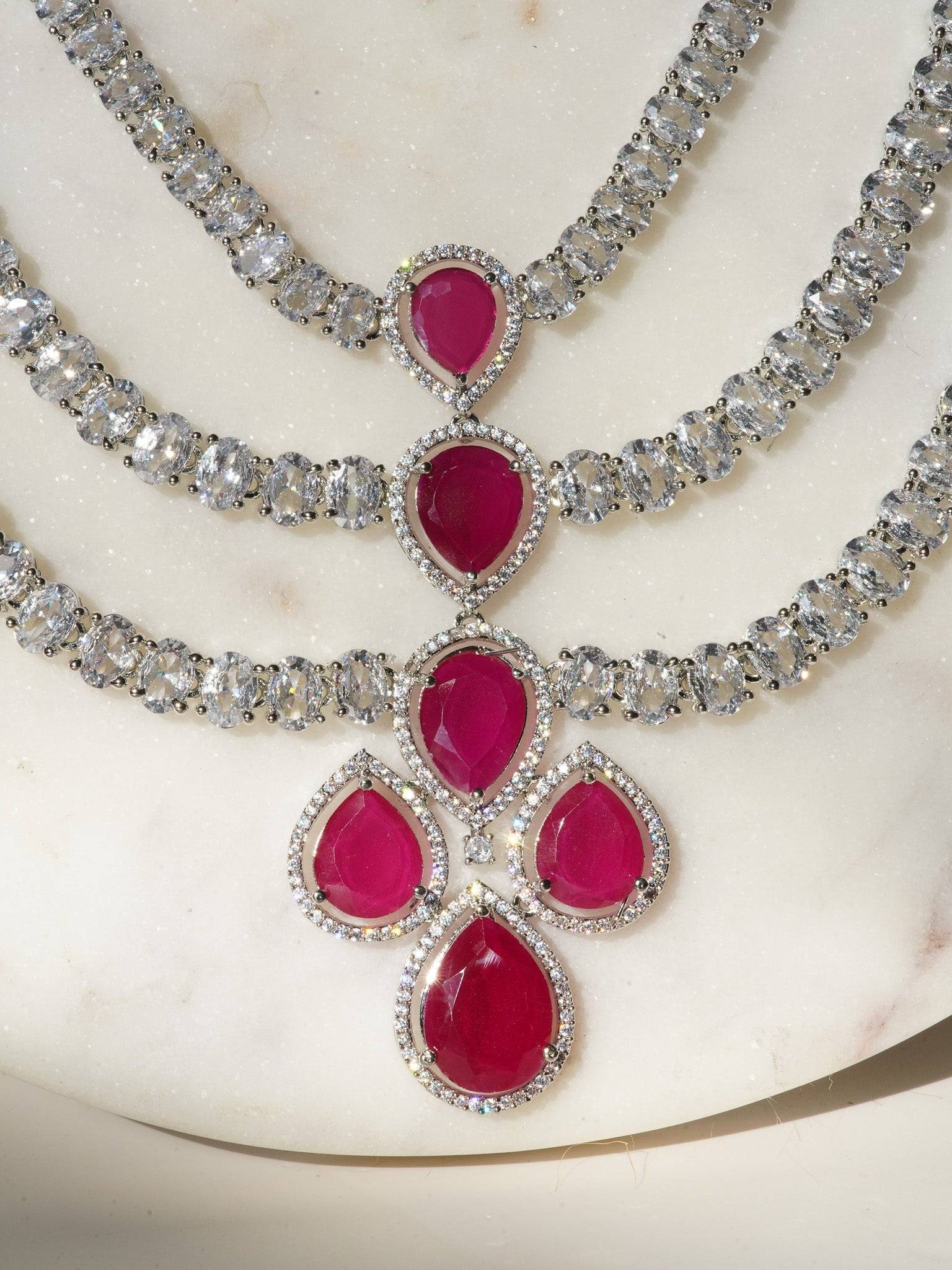 Niara Triple Layer Diamante Accent AD Necklace Set in gold or rhodium-plated silver finish with color options of silver & sapphire blue, silver & green, gold & green, and silver & ruby, featuring triple-layered chain links and matching statement earrings.