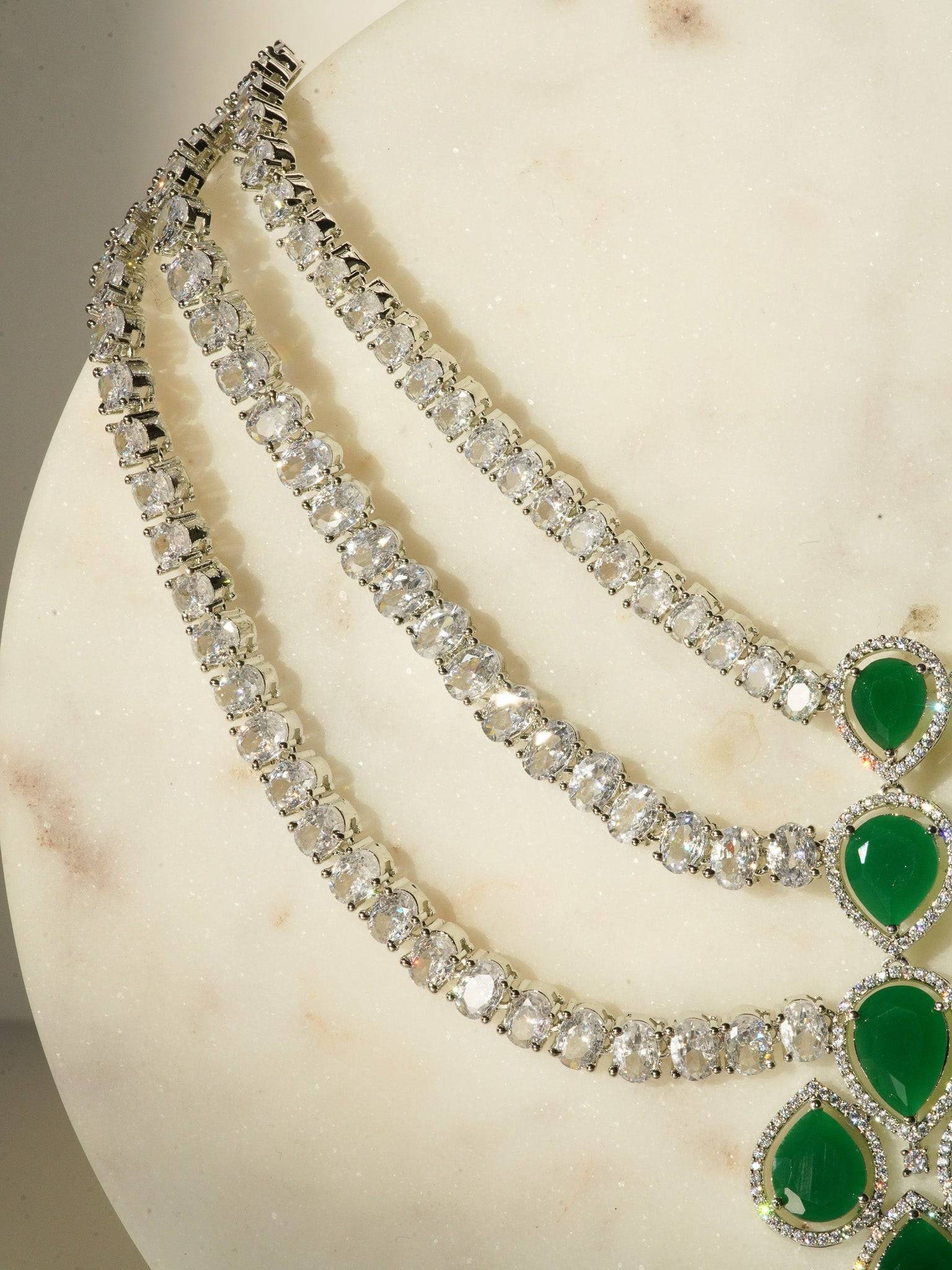 Niara Triple Layer Diamante Accent AD Necklace Set in gold or rhodium-plated silver finish with color options of silver & sapphire blue, silver & green, gold & green, and silver & ruby, featuring triple-layered chain links and matching statement earrings.