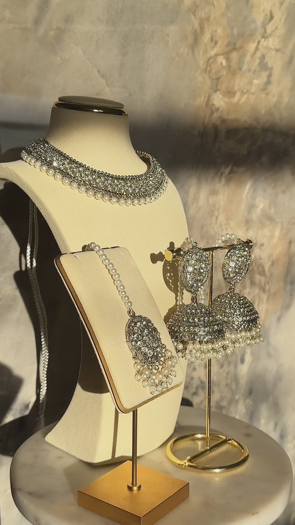 Urooj Necklace Set with pearl-accented choker, Jhumka earrings, and Maang Tikka on gold display stands. Handcrafted Pakistani jewelry.