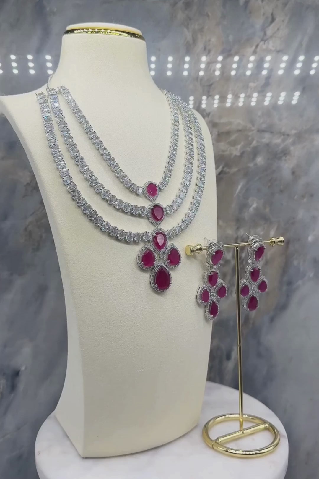 Niara Triple Layer Diamante Accent AD Necklace Set in gold or rhodium-plated silver finish with color options of silver & sapphire blue, silver & green, gold & green, and silver & ruby, featuring triple-layered chain links and matching statement earrings.