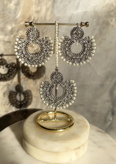 Antique gold Laila Chandbali Earrings and Maang Tikka Set with pearl rims, displayed on a gold stand with soft lighting.
