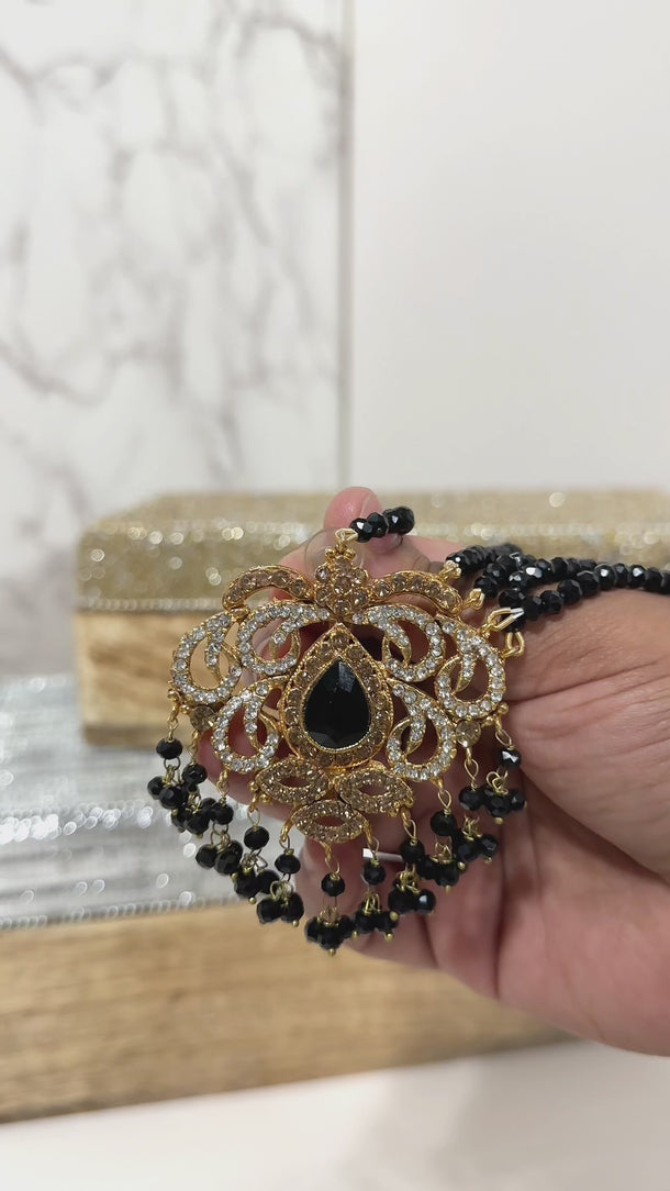 Handheld view of Ira - Chandbali earring with black beads and gold-tone finish, highlighting craftsmanship and CZ embellishments.