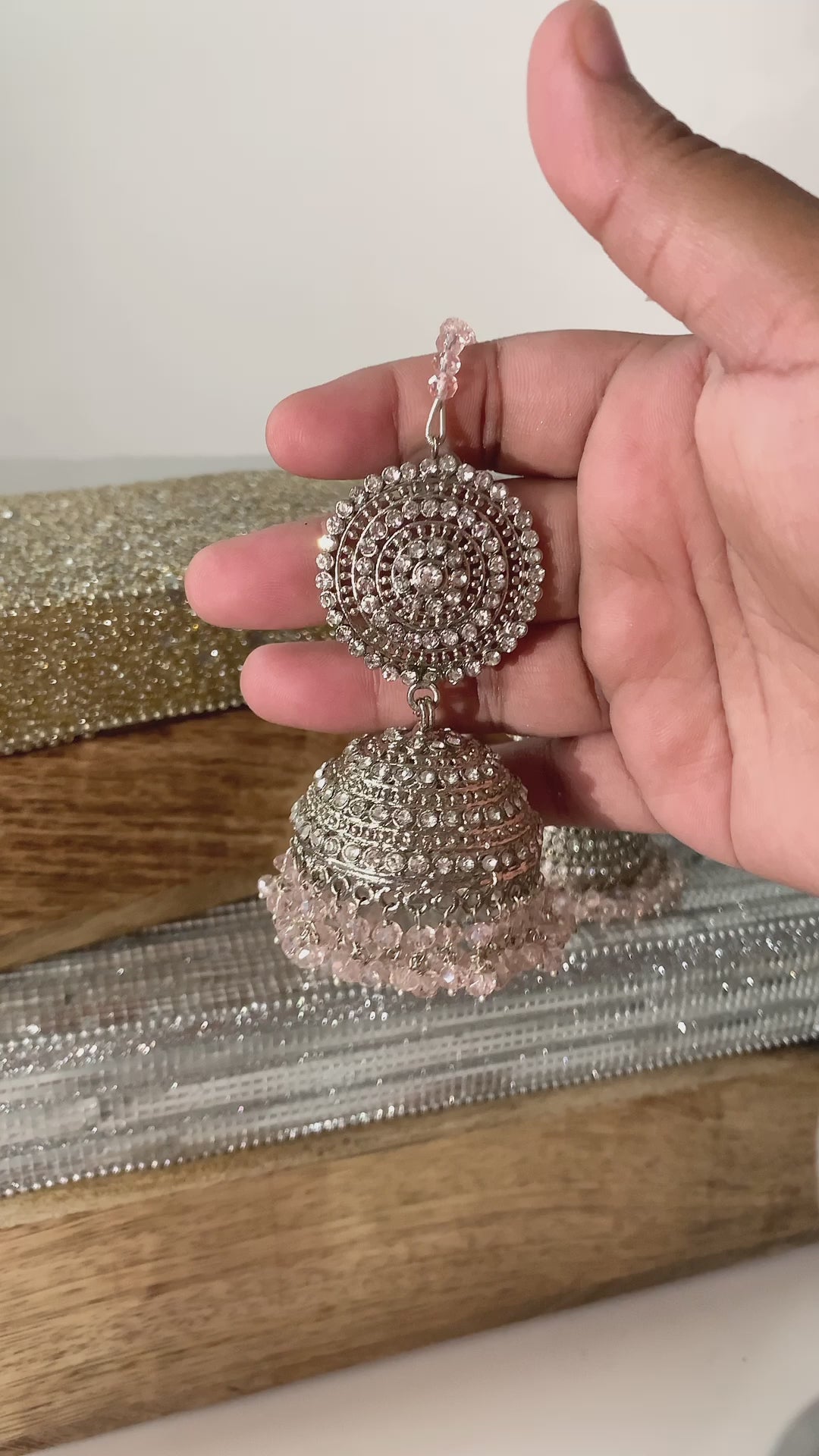 Handheld silver Tabiha Jhumka Earring with pink beads, showcasing detailed craftsmanship in traditional jewelry.