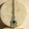 Rhodium-plated maang tikka with an emerald green center and teardrop-shaped white AD stones from Inaury