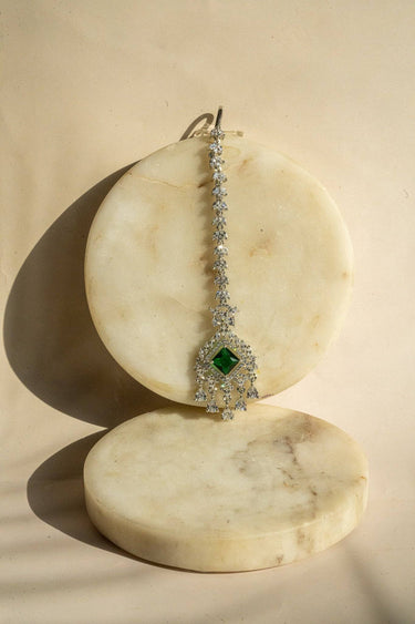Rhodium-plated maang tikka with an emerald green center and teardrop-shaped white AD stones from Inaury