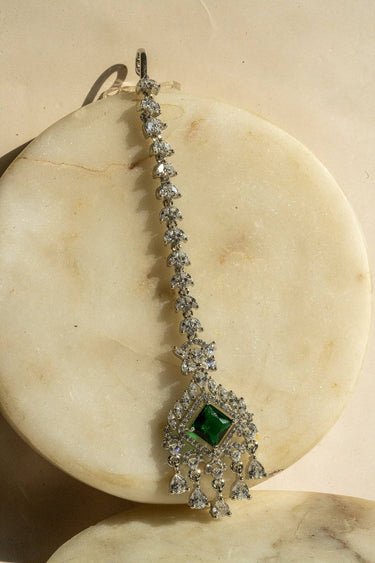 Rhodium-plated maang tikka with an emerald green center and teardrop-shaped white AD stones from Inaury