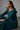 Sahara chandelier earrings worn by a seated model in a teal dress, full-length context view showing earring scale from stud to pearl drops at mid-neck