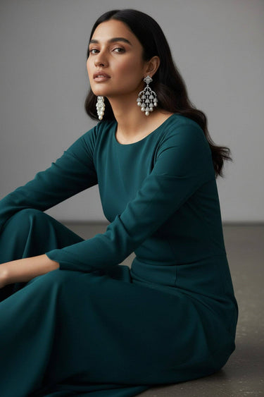 Sahara chandelier earrings worn by a seated model in a teal dress, full-length context view showing earring scale from stud to pearl drops at mid-neck