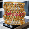 Tavisha 11-piece gold-plated floral and pearl bangle set with green and ruby accents.