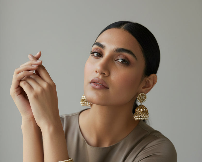 Woman wearing gold jhumka earrings against a neutral background