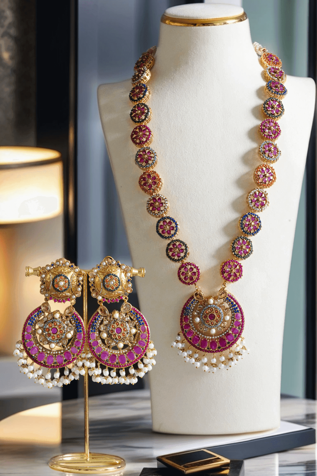 Adiva Necklace Set - Gold Mala with multi-color stones and pearl drops, displayed on a bust with matching statement earrings on a stand.