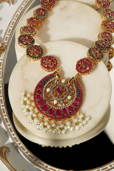 Adiva Necklace pendant with vibrant pink stones and pearl accents, resting on a decorative mirrored surface.