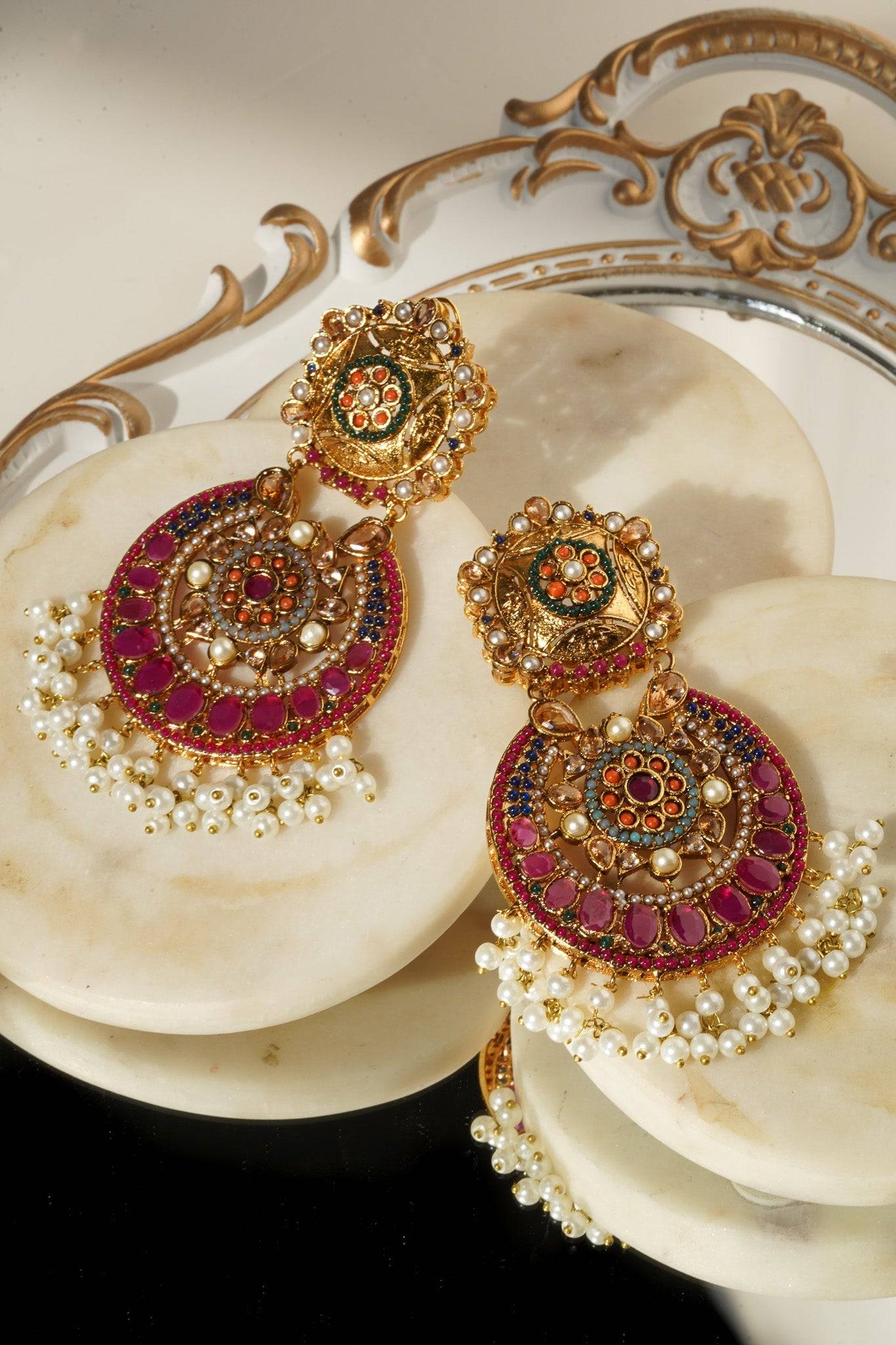 Adiva Earrings with ornate gold design, red and green stones, and pearl fringe, styled on a marble tray.
