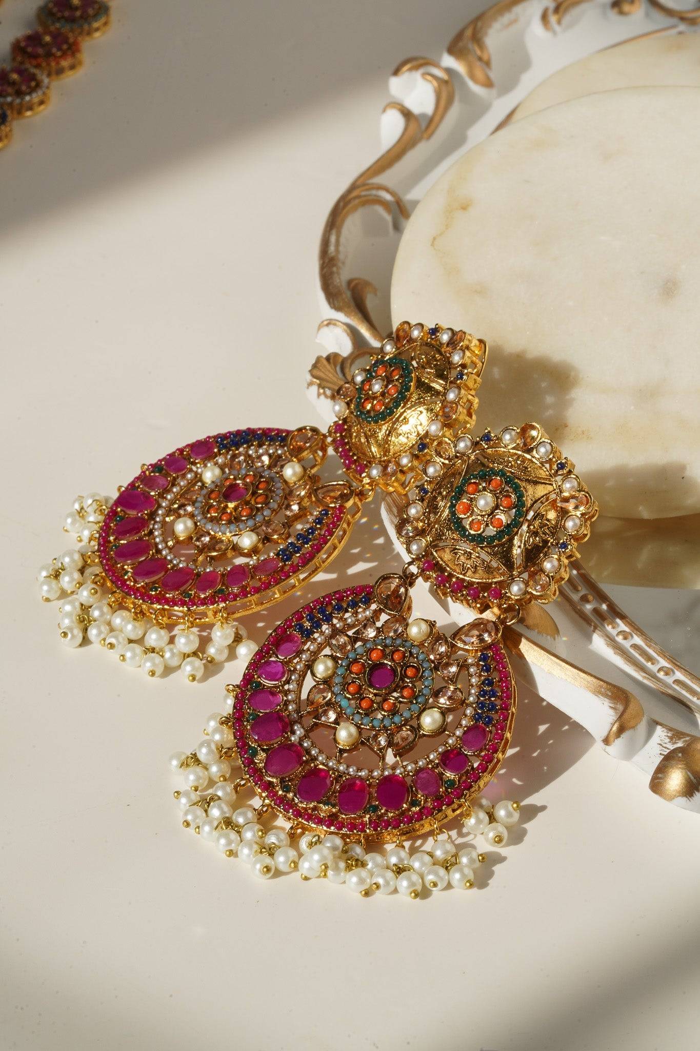 Side view of Adiva Earrings with gold plating, multi-color stones, and pearl accents, arranged near necklace.