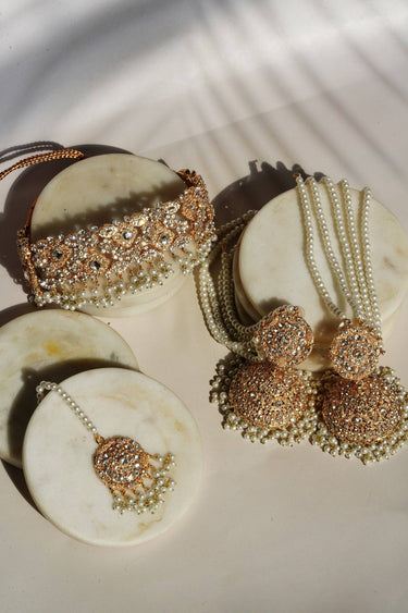 Maang Tikka from Ayesha Choker Necklace Set with white pearls and gold floral design, styled on a marble background.