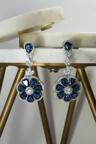 Chahat Floral AD Earrings in blue with rhodium finish. Elegant drop design with floral motif and sparkling stones.