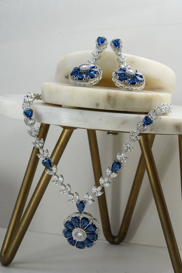 Chahat Rhodium Floral AD Necklace Set in blue displayed on marble and gold stand. Includes matching floral earrings.