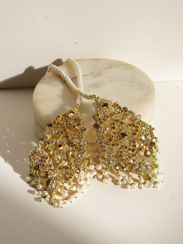 Esmeray Gold Earrings and Maang Tikka set with pearl strands and intricate filigree, styled on a marble platform.