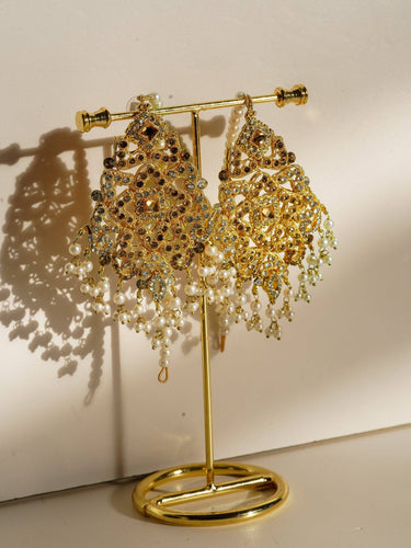 Pair of Esmeray Gold Dangler Earrings with pearl drops and crystal accents, displayed on a gold stand for jewelry showcase.
