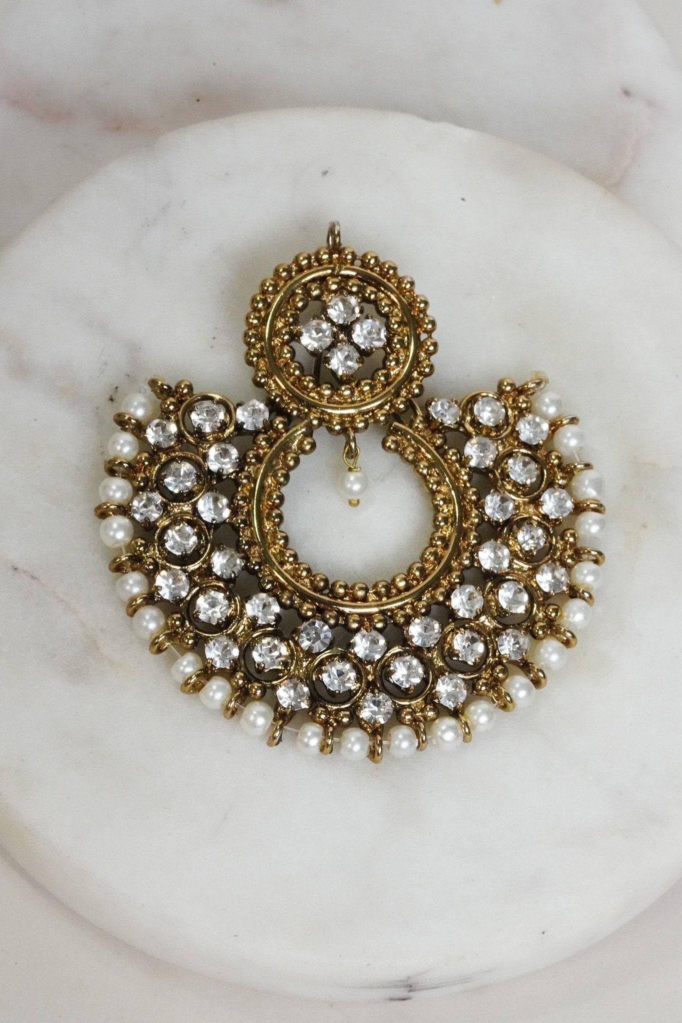 Laila Chandbali Earring in antique gold with circular patterns, white stones, and pearl detailing, placed on white marble.