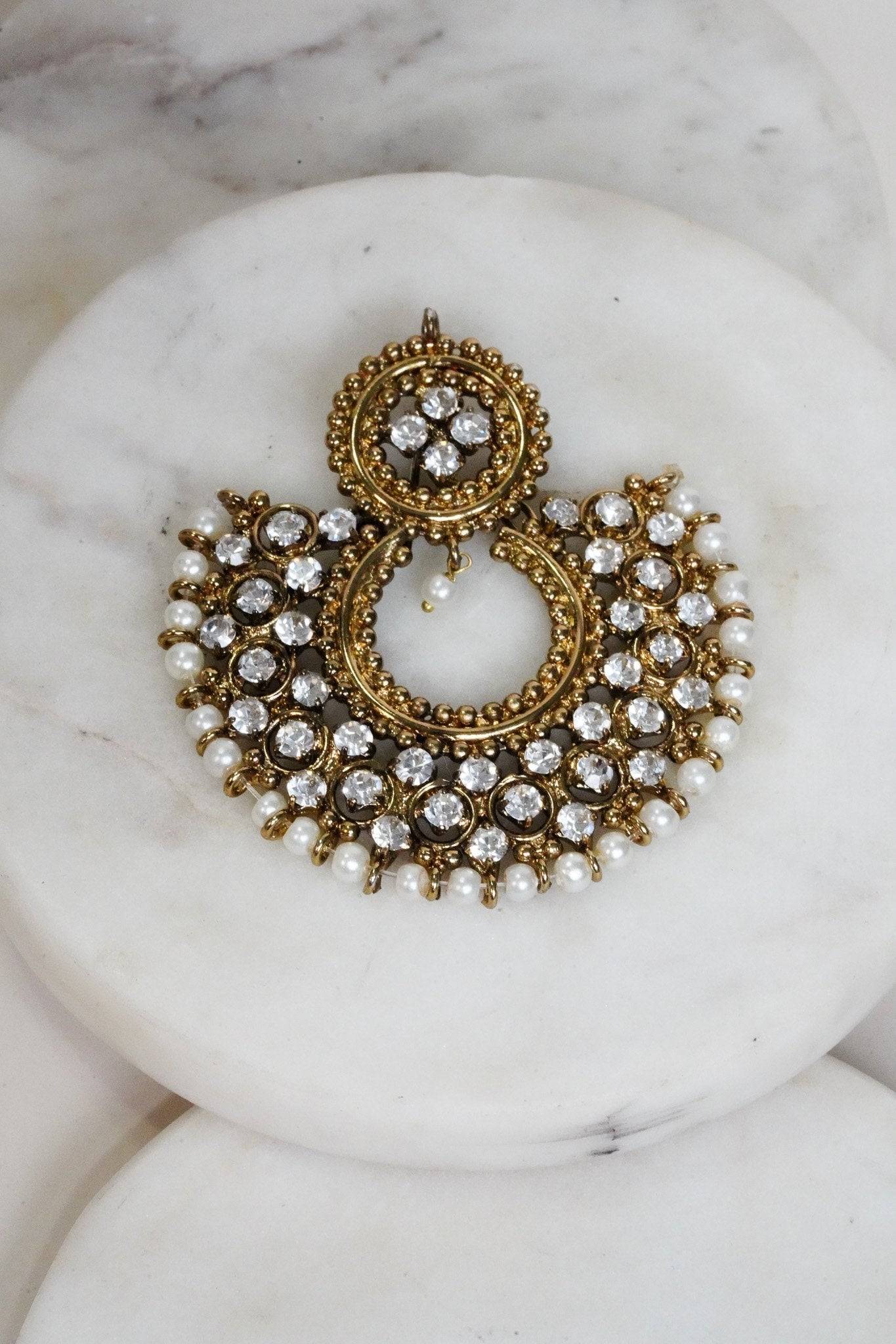 Top view of Laila Chandbali Earring in antique gold with pearl accents and white stones, styled on layered marble slabs.