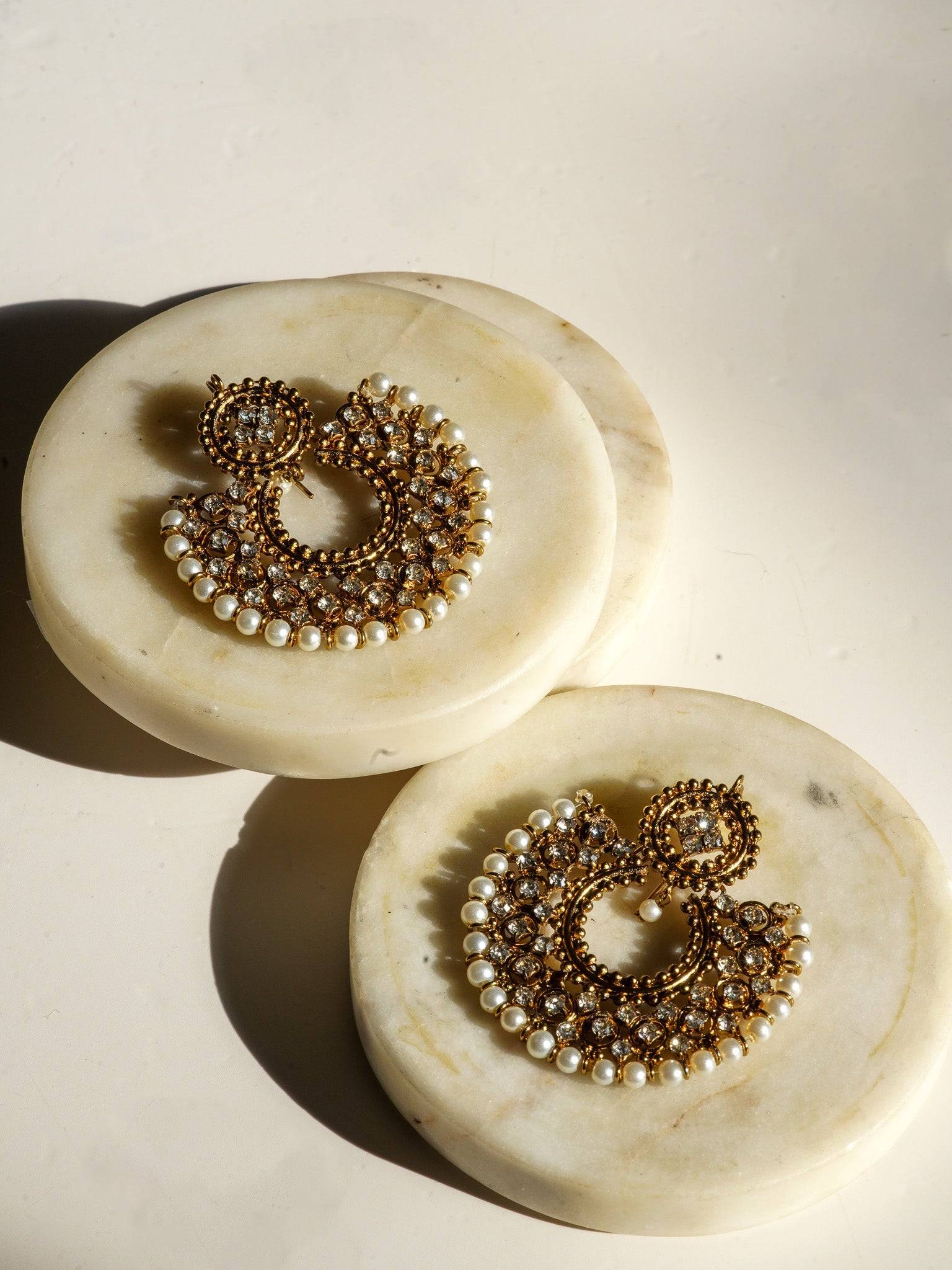 Pair of Laila Chandbali Earrings in antique gold with pearl rims, placed on marble slabs for a refined jewelry showcase.