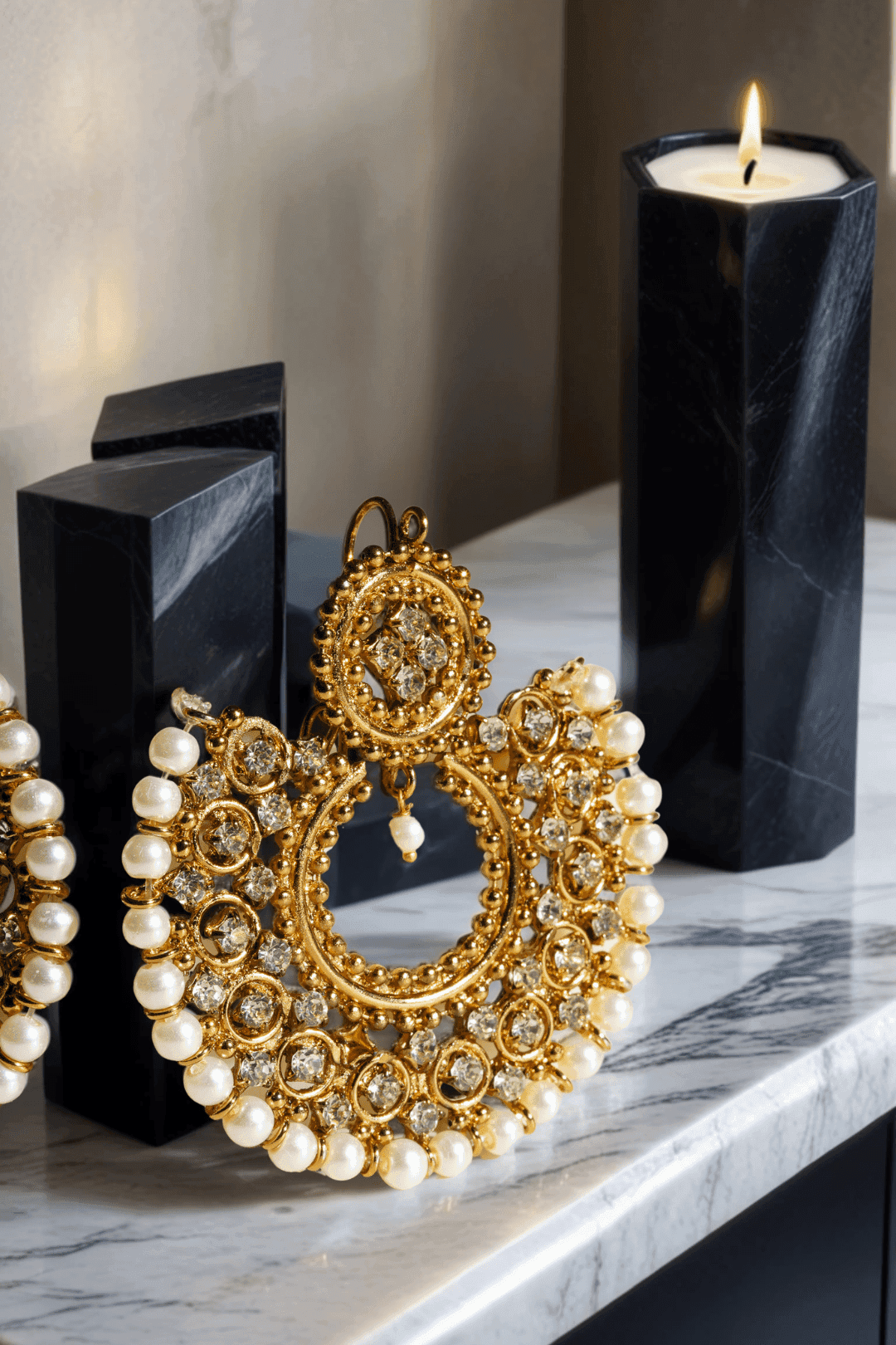 Single Laila Chandbali Earring in antique gold with pearl accents, styled with a black candle for a dramatic jewelry display.