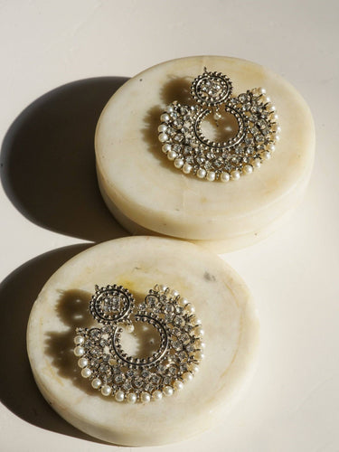 Laila Chandbali Earrings and Maang Tikka Set in antique gold with white stones and pearl edging, displayed on round marble slabs.
