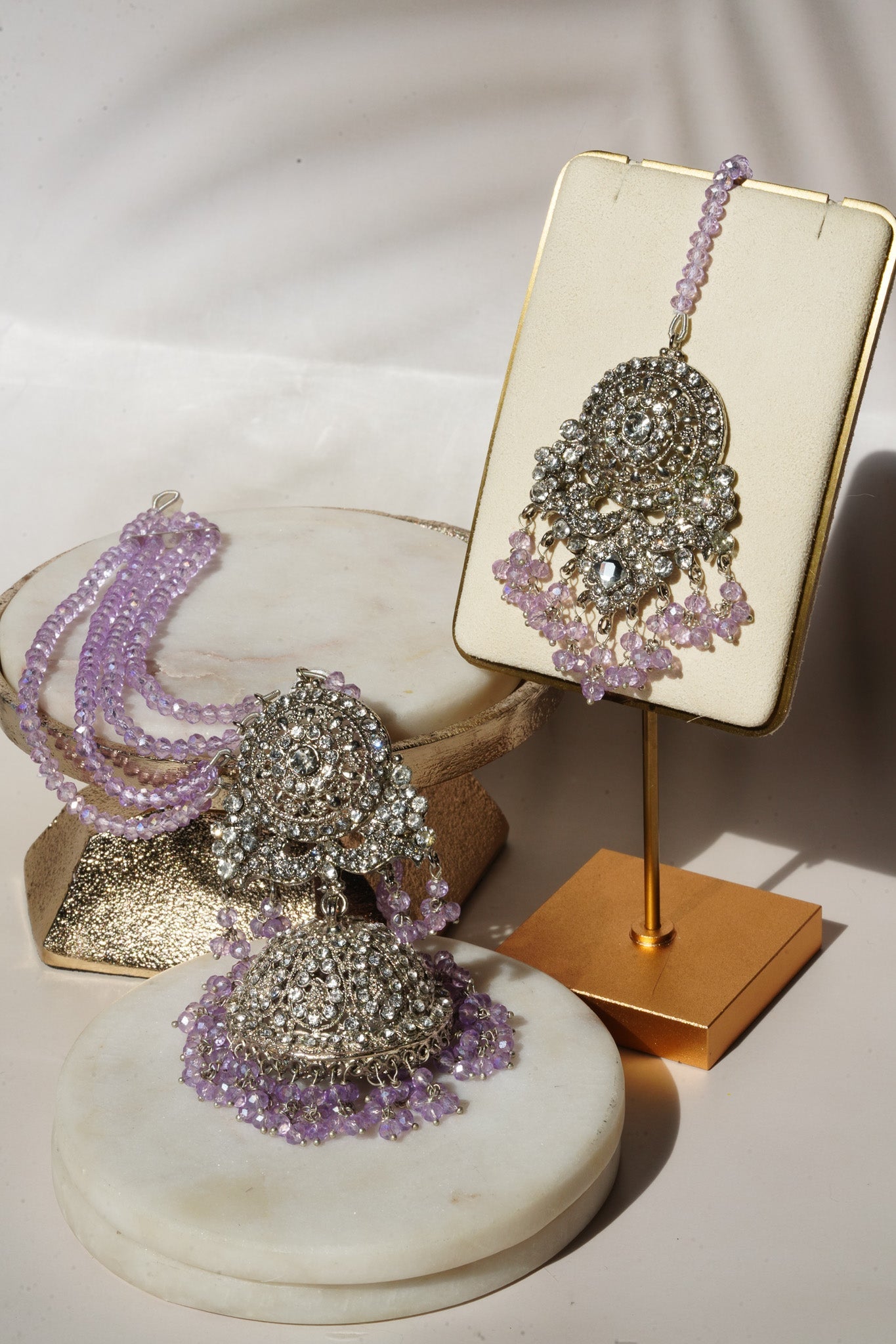 Lavender beaded earrings and maang tikka from Namar Choker Necklace Set displayed on marble and gold stands.