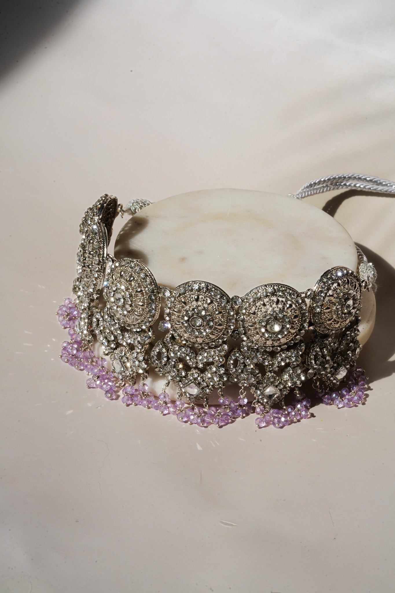 Side view of lavender beaded choker from Namar Silver Plated AD Indian Choker Necklace Set on marble base.