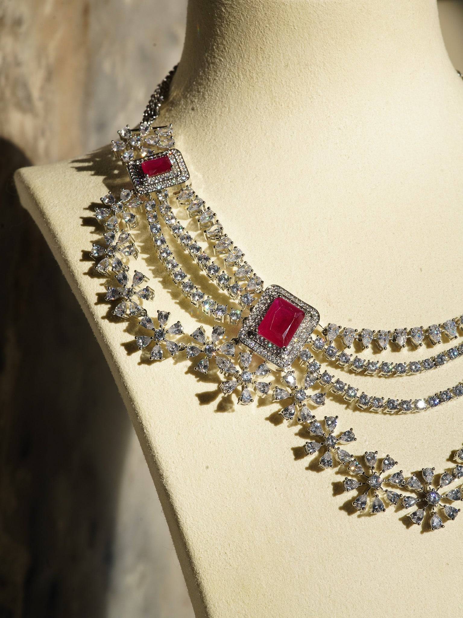 Neha Diamanté Accent Classic Necklace Set - Rhodium-plated with ruby or green accents, floral pattern, curvy layers, and matching 2-inch earrings.