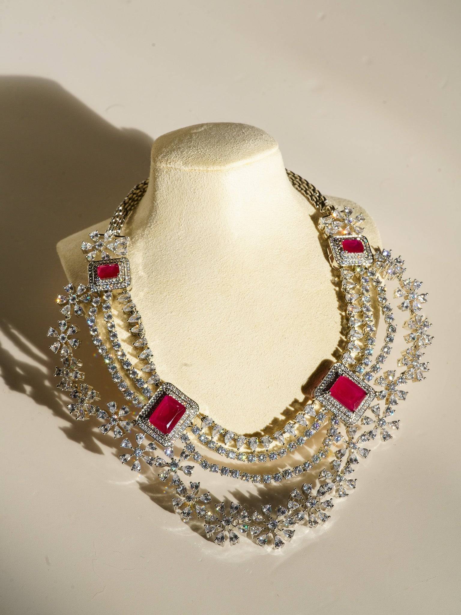 Neha Diamanté Accent Classic Necklace Set - Rhodium-plated with ruby or green accents, floral pattern, curvy layers, and matching 2-inch earrings.