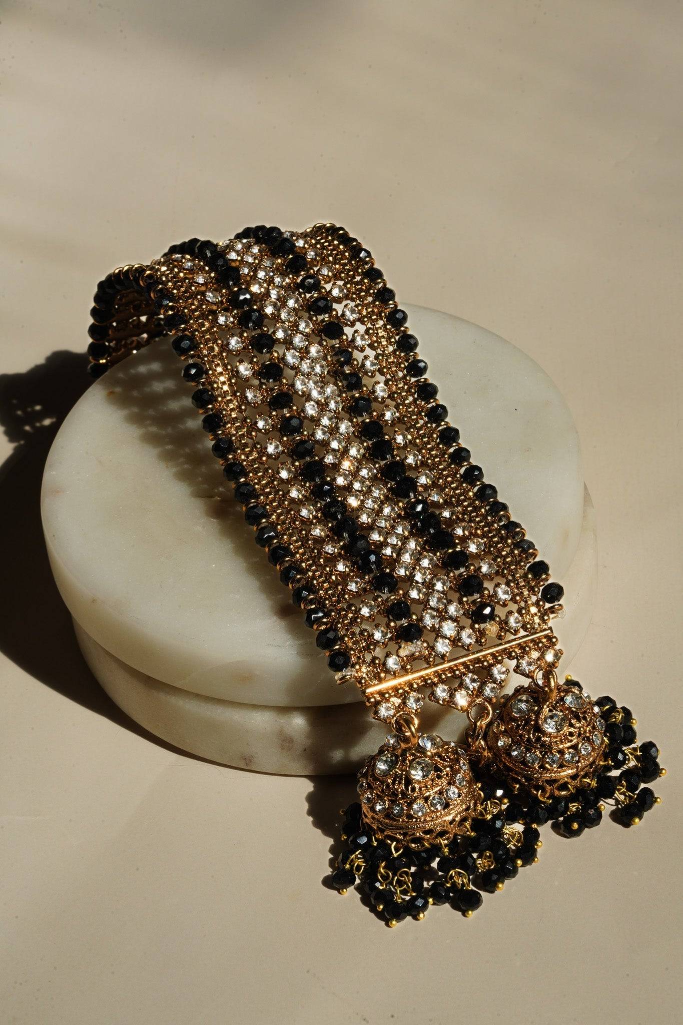 Full view of Samia Bangles in gold with black bead and CZ stone accents, finished with ornate jhumkas, laid on marble.