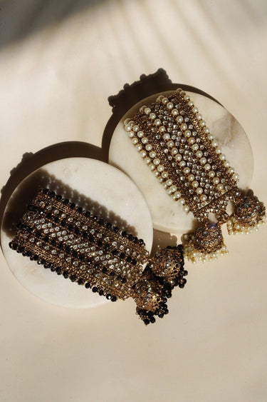 Two Samia Bangles sets in gold with pearl and black bead options, featuring jhumkas and CZ stones, laid flat on marble surface.