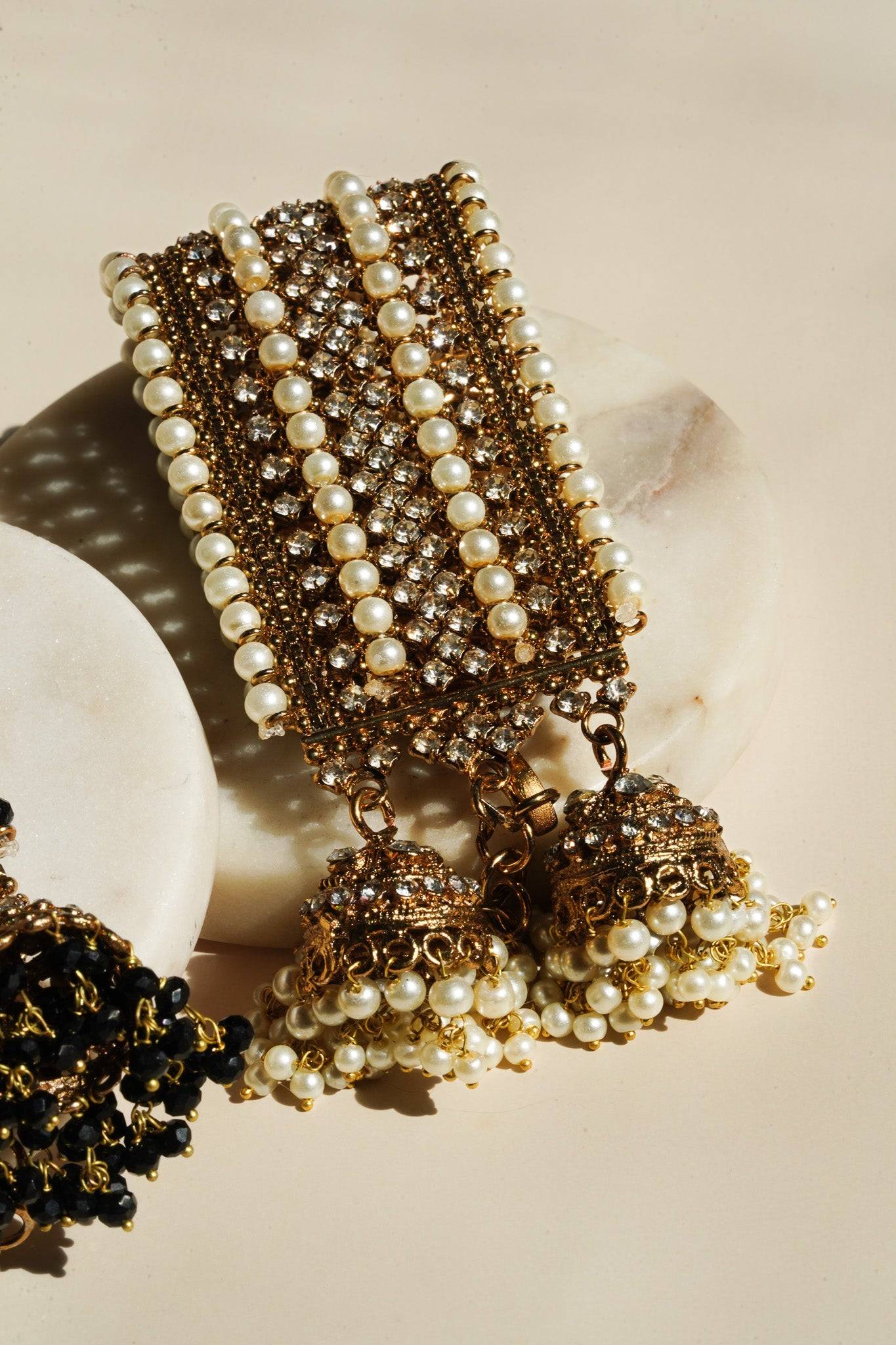 Samia Bangles in gold with pearl and CZ stones, paired with dual jhumkas, displayed on marble for a luxurious presentation.