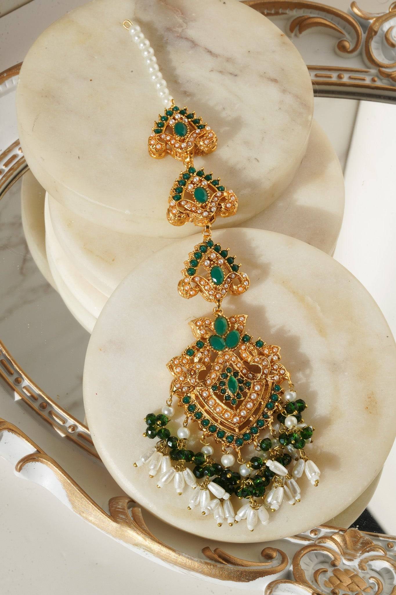 Close-up of green stone Maang Tikka from Sanjana Set with pearl drops and gold filigree, exuding cultural richness.