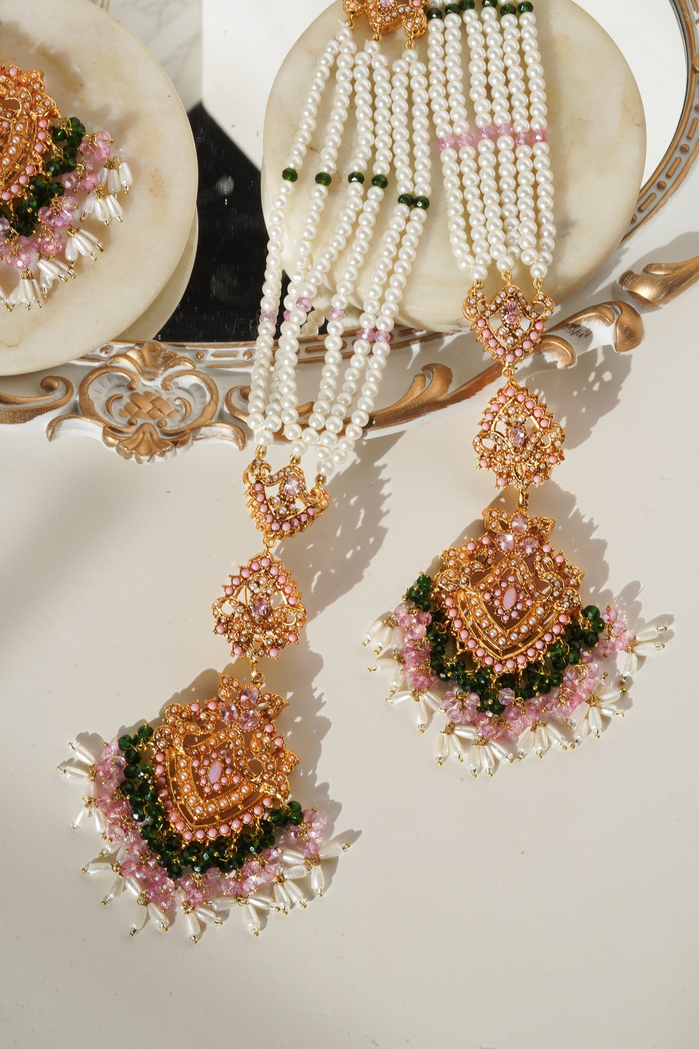 Close-up of pink stone Maang Tikka from Sanjana Set with pearl and green bead fringe, exuding cultural charm.